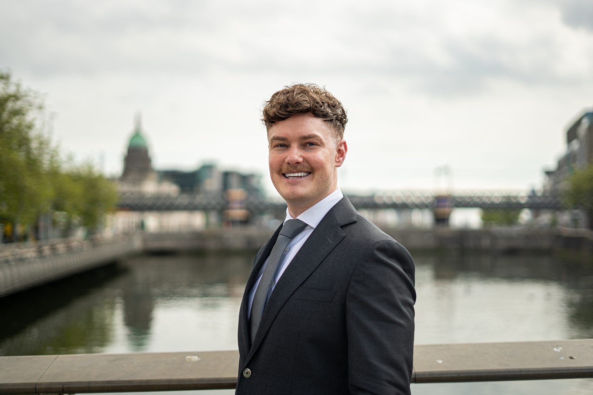 Professional portrait of a man in a dark suit by the Liffey